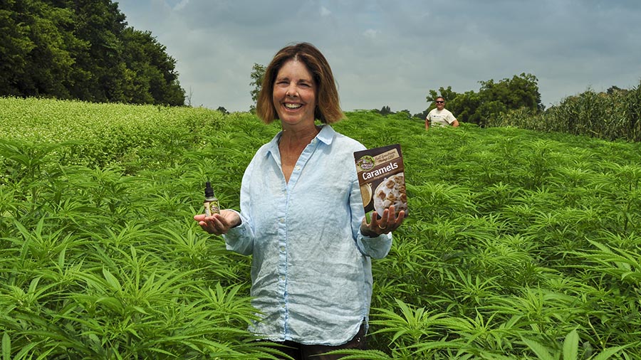 Laura Freeman standing in organic hemp field holding Homestead Alternatives Full Spectrum CBD Oil and Caramels.