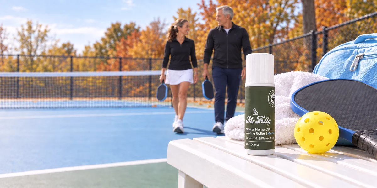 Mt. Folly CBD Cooling Roller in sharp focus beside pickleball gear, with a woman in a black shirt and a taller older man in a black jacket softly blurred on an autumn court
