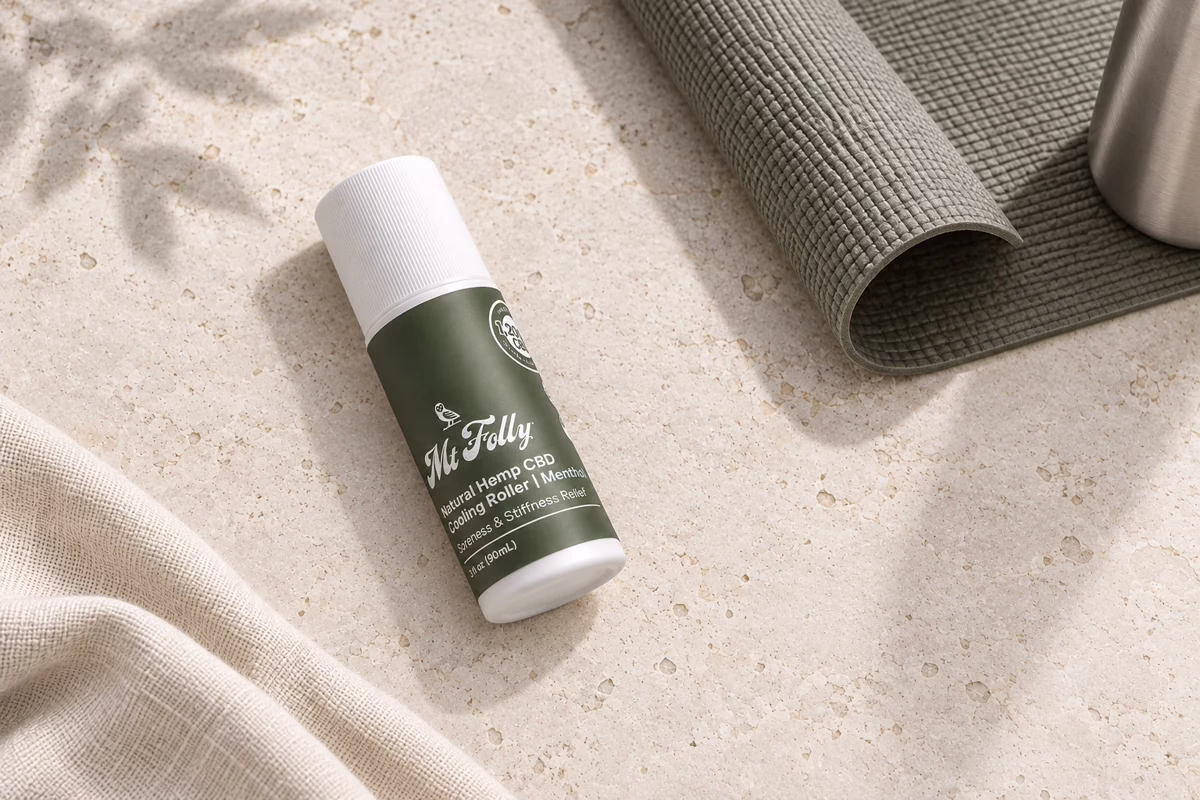 Mt. Folly CBD Cooling Roller beside a partially unrolled olive yoga mat and brushed-metal bottle on pale stone